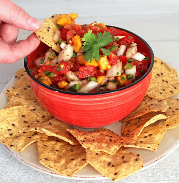 a hand dipping a chip into a bowl of Homemade Salsa with Tomatoes and Mango