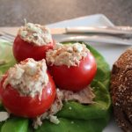 Three tomatoes stuffed with tuna salad on fresh lettuce with a piece of bread on a white plate