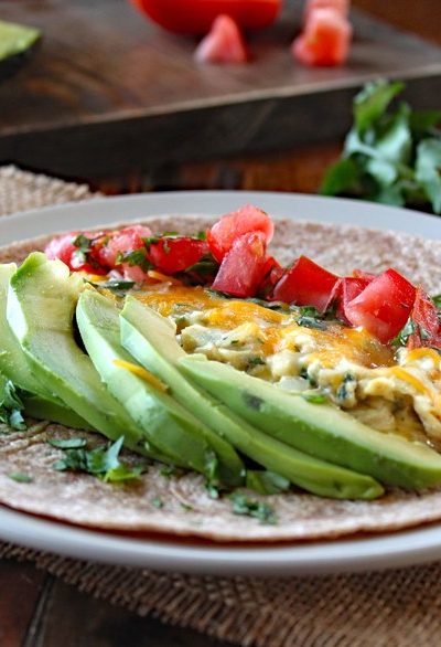 Breakfast Burrito with Eggs, Tomato, and Avocado on a white plate ready to be rolled up