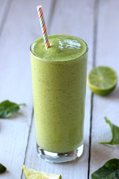 Green Smoothie with Pineapple and Mango with a straw and some limes scattered around