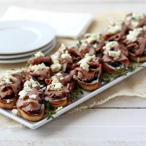 roast beef crostini with dried figs and blue cheese on white plate