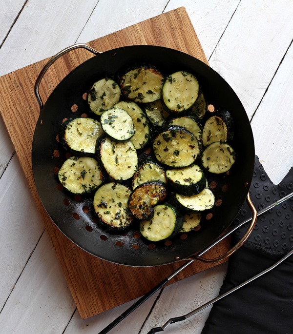 grilled zucchini in a grill basket on wood cutting board