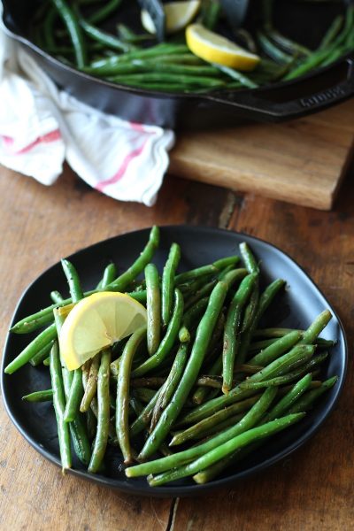 Cooked green beans on black plate with lemon slice