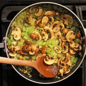 chopped onions, celery, and mushrooms in sauce pan with wooden spoon