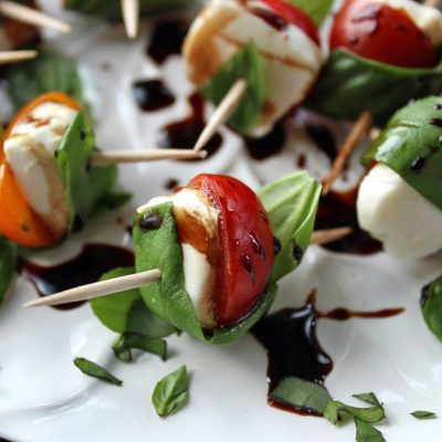 Cherry tomatoes and fresh mozzarella wrapped with fresh basil leaves on white plate