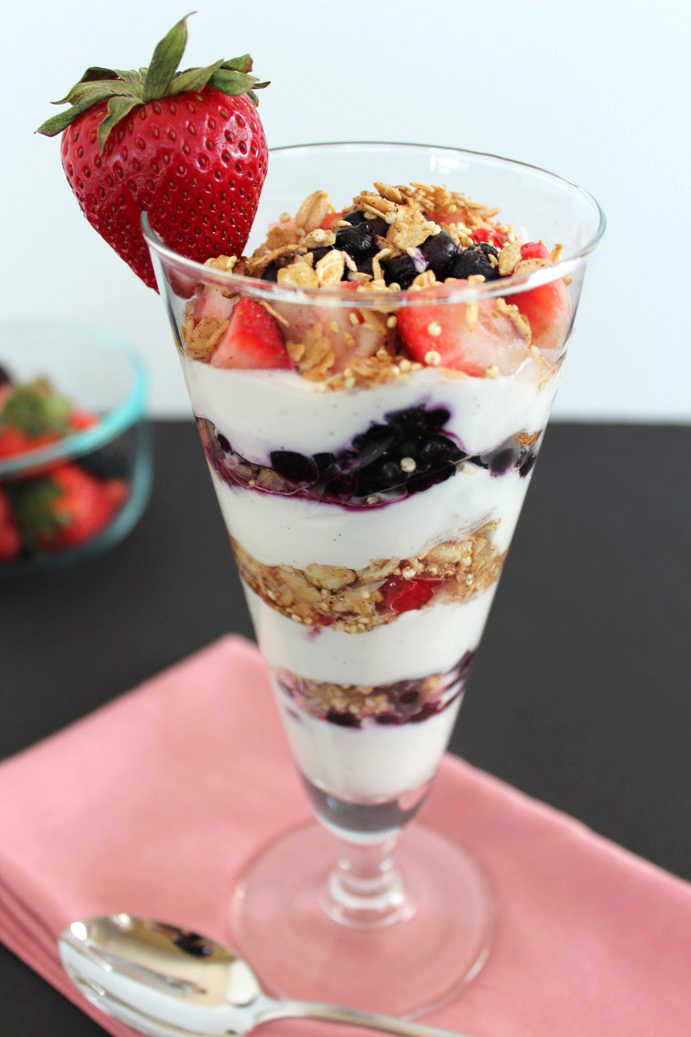 yogurt and berries layered with granola in clear fluted glass