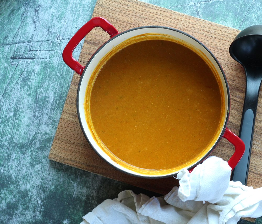 Blended red lentil soup in pot on wood cutting board
