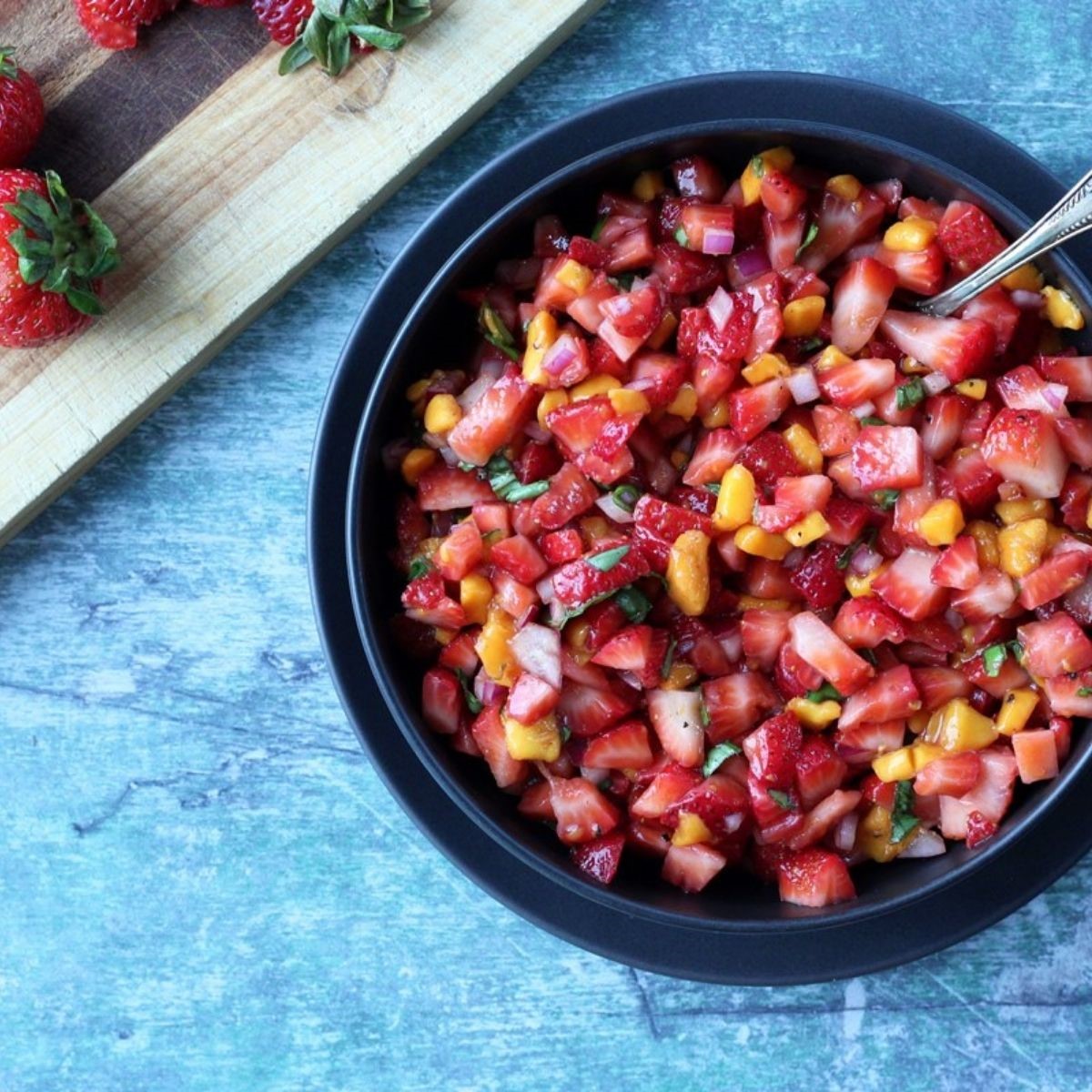 Diced strawberries, onions, and mango as a salsa in a black bowl
