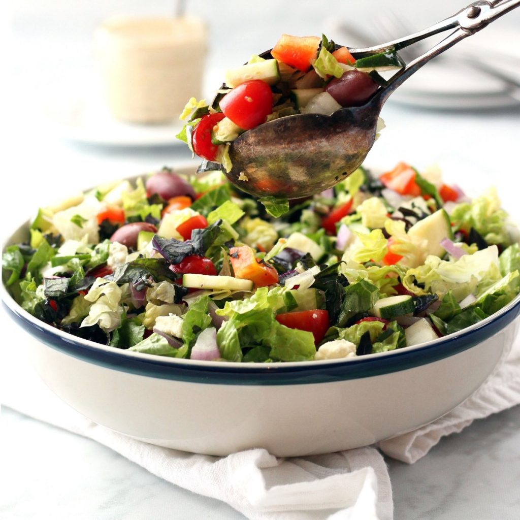 chopped salad being scooped out of a white bowl with salad tongs