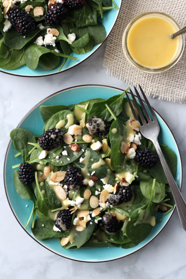 Spinach Salad with blackberries, feta cheese, almonds and dressing on a teal plate, looking down on it from above,