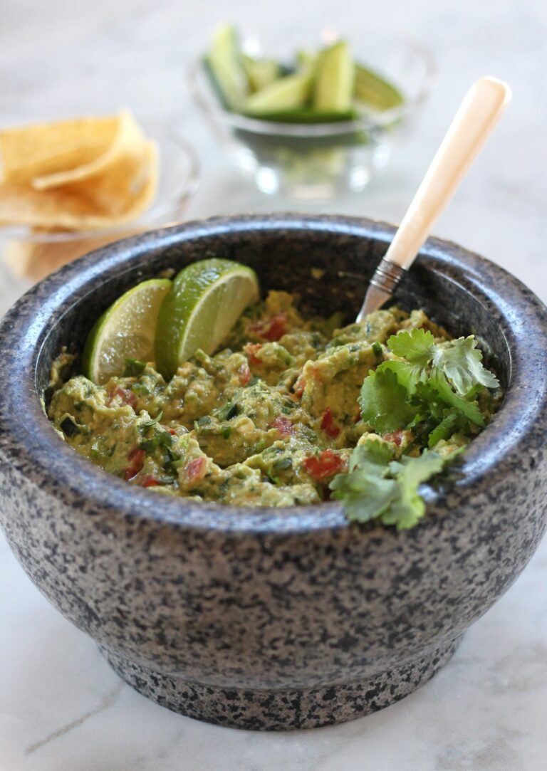 Guacamole in stone bowl with chips and cucumber in background